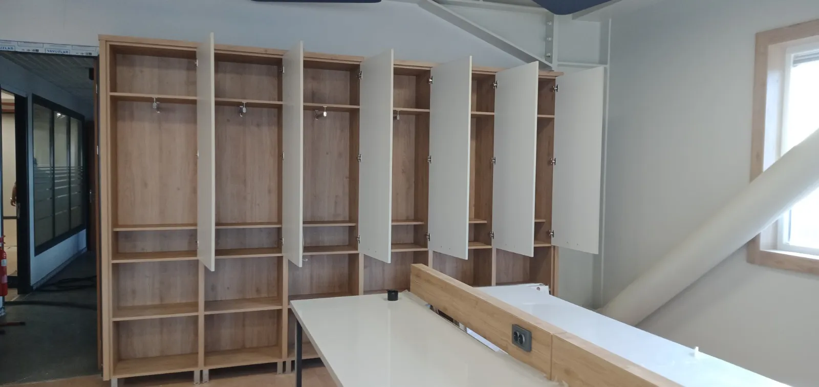 Açık meşe görünümlü boy dolap sırası, kapakları açık halde montaj anı