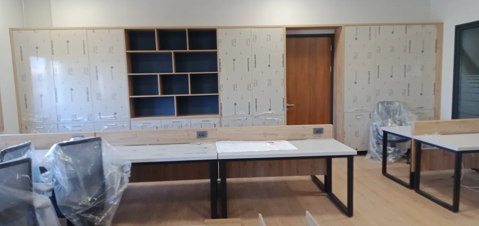 Ofiste duvar boyu dolap ünitesi, çekmeceli alt modül ve lacivert arkalıklı açık raflar