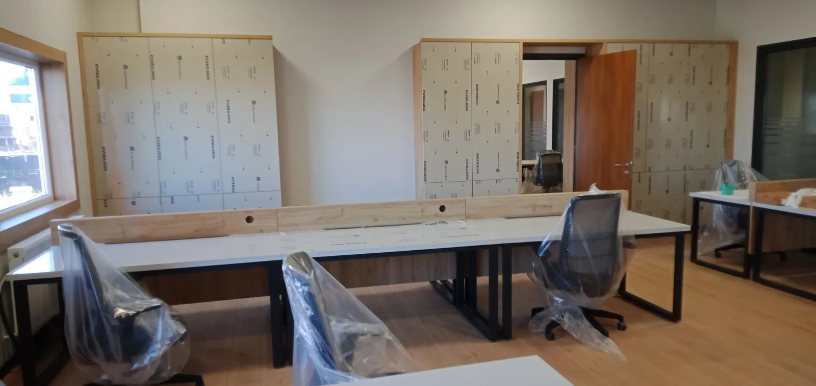 Ofis odasında boy dolap sırası ve siyah ayaklı beyaz çalışma masaları