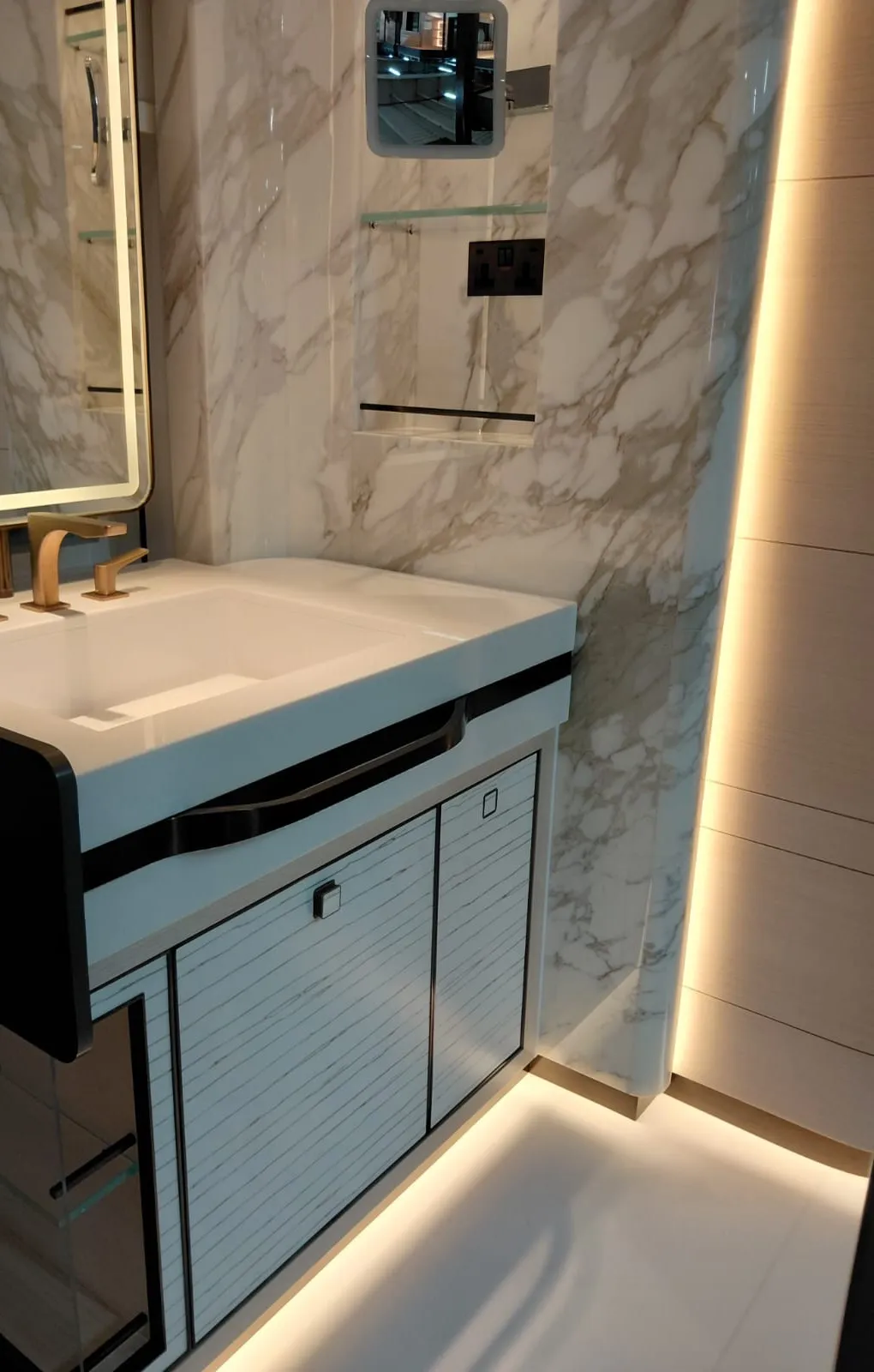 Yakın açıdan beyaz tezgahlı lavabo dolabı, altın armatür ve çizgi desenli kapak yüzeyleri