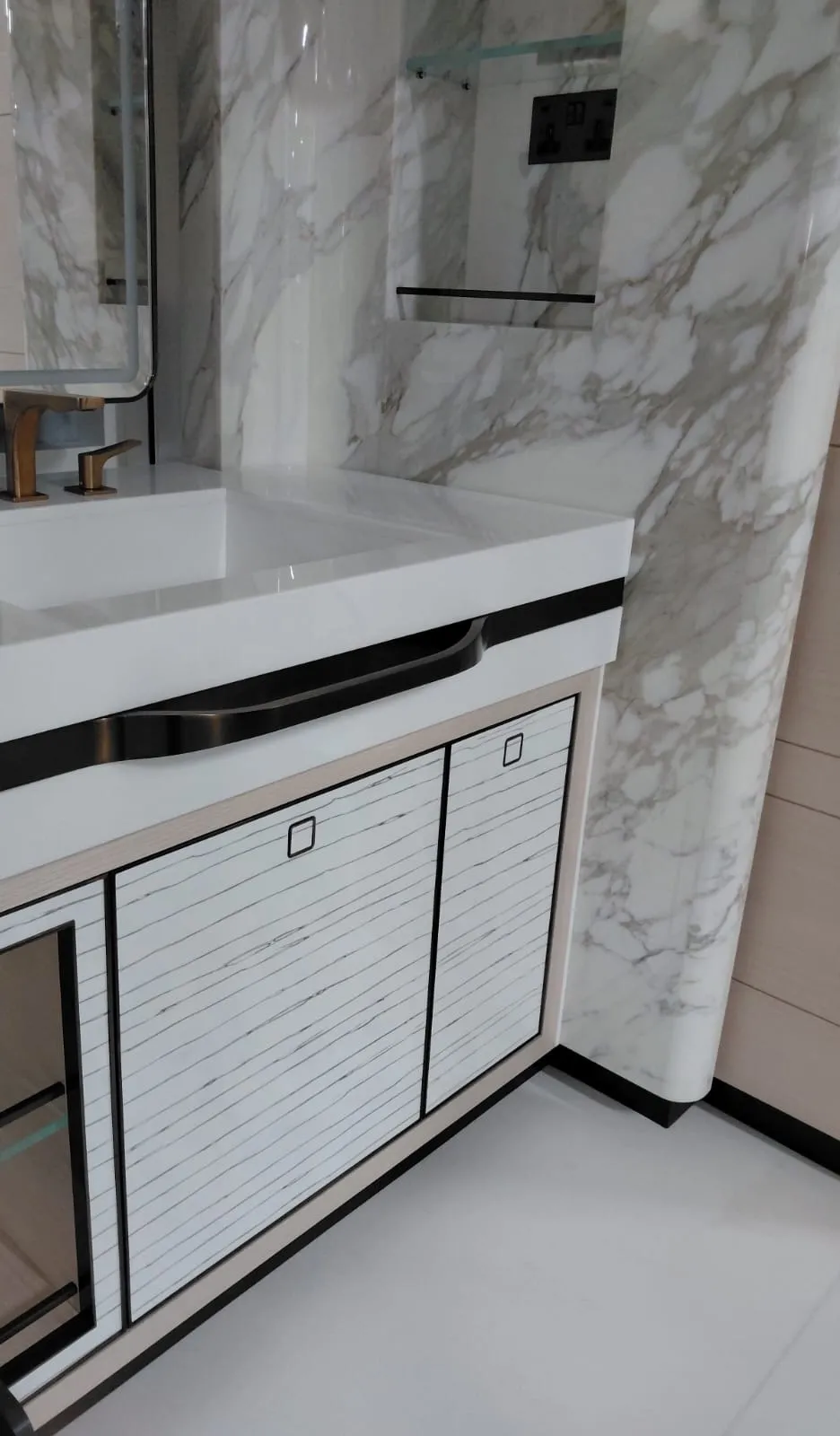 Taş görünümlü duvar önünde beyaz lavabo tezgahı ve çizgili desenli banyo dolabı