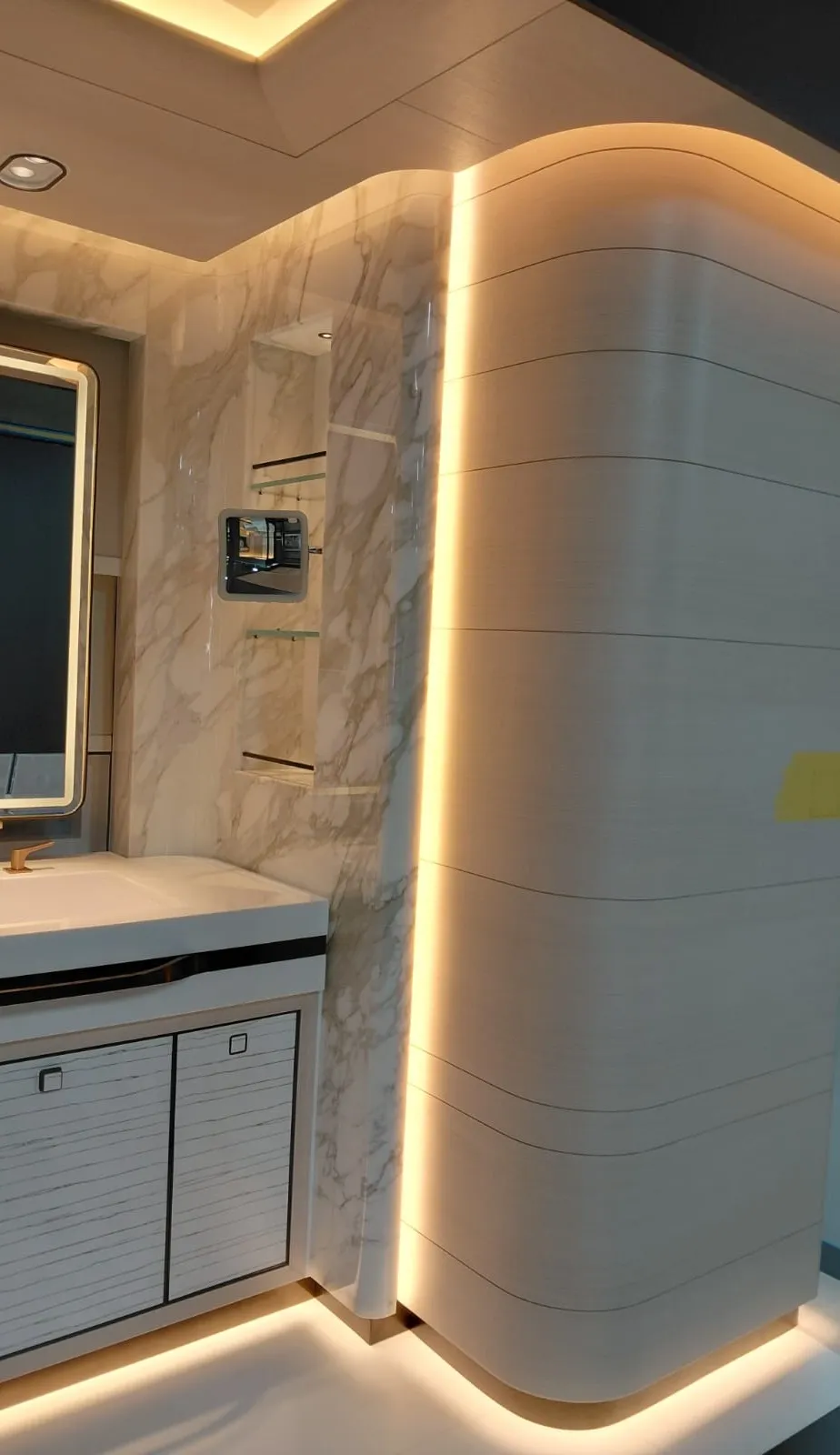 Taş görünümlü duvarlı banyoda aydınlatmalı ayna, tezgah altı dolap ve kavisli yivli panel