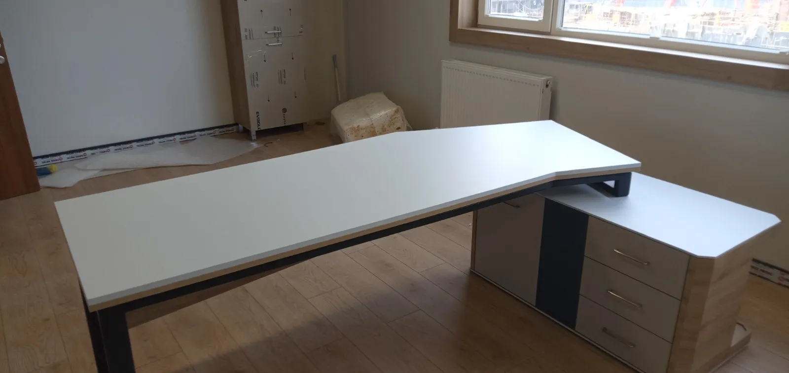 Geniş beyaz tablalı yönetici masası ve çekmeceli keson, pencereli ofis odasında